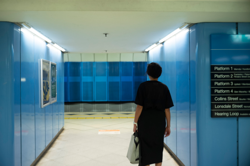 Woman dressed in black walking through a blue-walled train station.